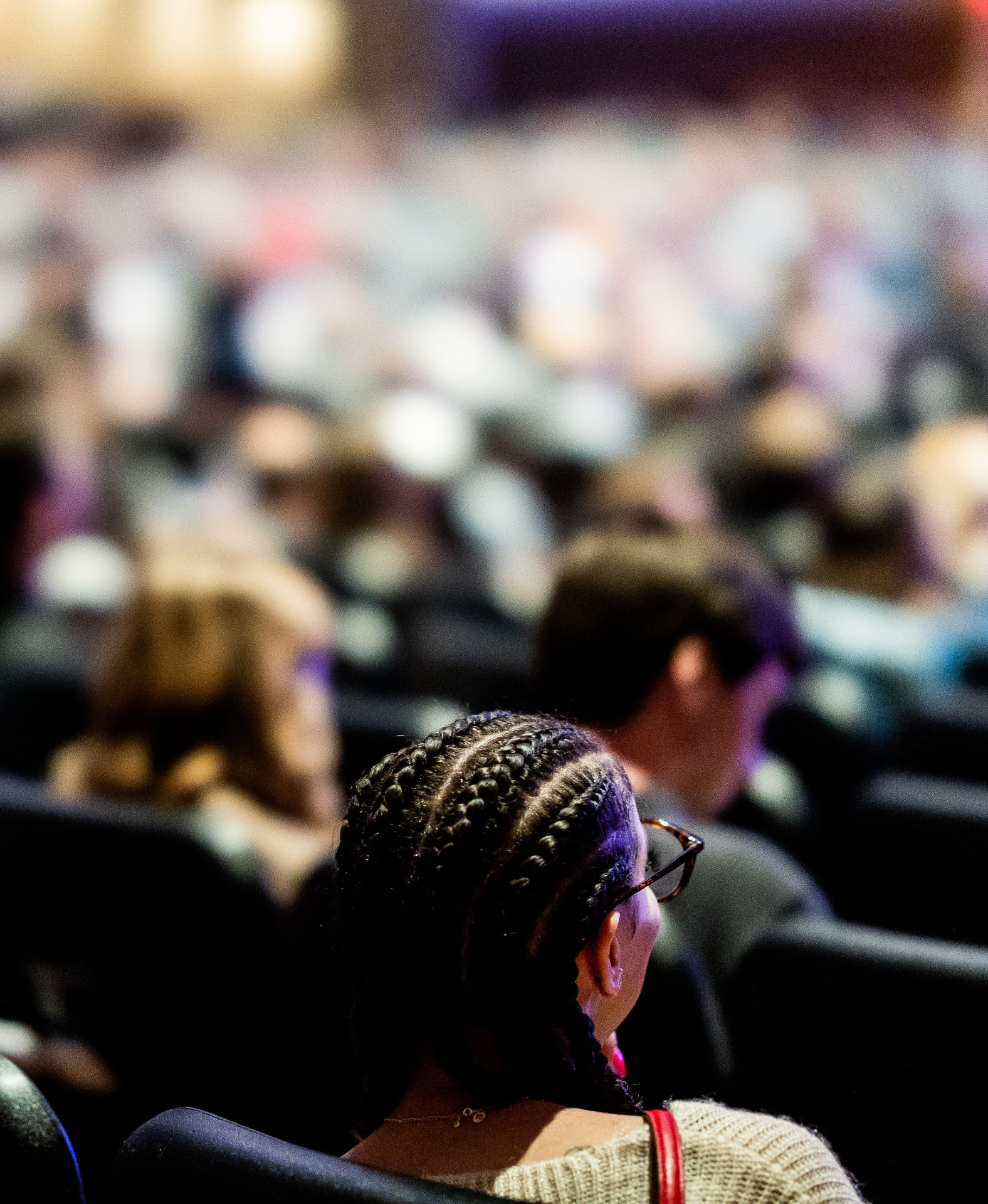A person seated in an audience facing a stage